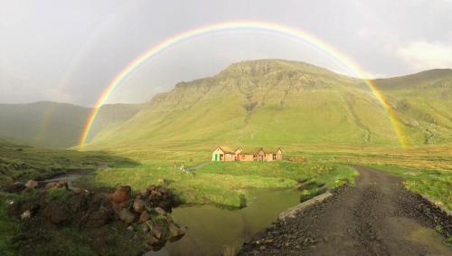 a rainbow over a house in the middle of a field at Múlafossur Cottages by famous waterfall in Gásadalur in Gásadalur