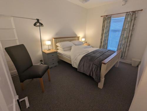 ein Schlafzimmer mit einem Bett, einem Stuhl und einem Fenster in der Unterkunft Cape Cottage in Glyncorrwg