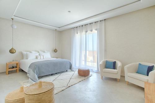 a white bedroom with a bed and a chair at L'Orientale By La Siredrah in Marrakech