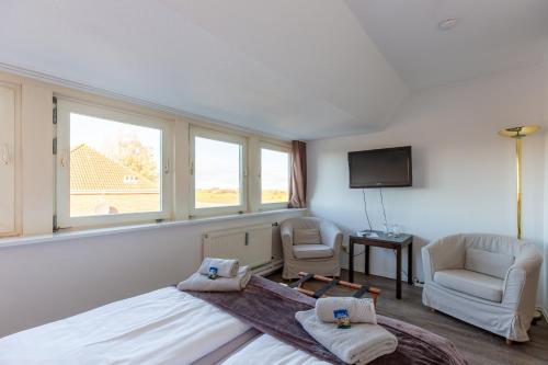 a bedroom with a bed and two chairs and a tv at Hotel MeerLand Pellworm in Pellworm