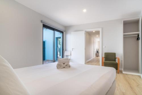a white bedroom with a large bed and a chair at Buzz Apartment in Jardim do Mar