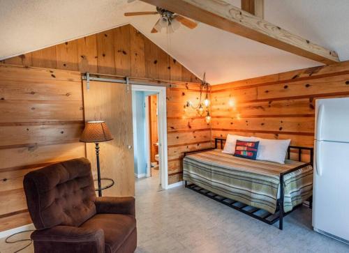 Schlafzimmer mit Holzwänden, einem Bett und einem Stuhl in der Unterkunft Big Blue Lake Cottages, LLC - Cottage #1 in Holton