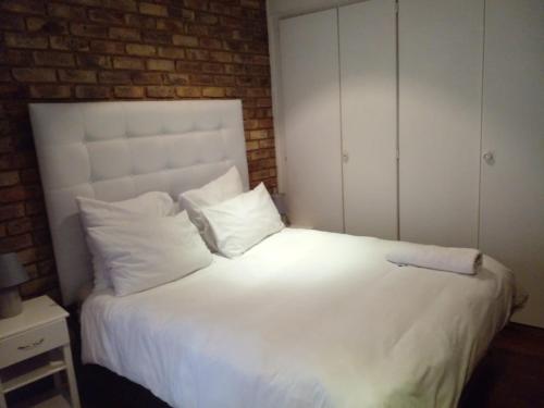 1 cama blanca con almohadas blancas y pared de ladrillo en Tshidiso Guesthouse, en Centurion