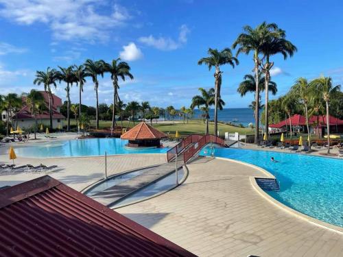- une piscine avec des palmiers et l'océan dans l'établissement TI OASIS vue Mer dans village Pierre & Vacances, à Sainte-Luce