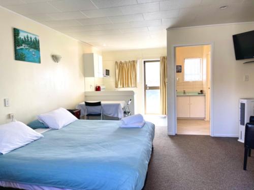 a bedroom with a large blue bed and a kitchen at Dukes Midway Lodge in Auckland