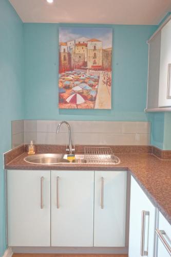 a kitchen with a sink and a painting on the wall at Soak up the Light at a Soothing, Stylish Apartment in Swansea Marina in Swansea