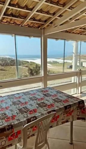 een tafel en een stoel in een kamer met ramen bij Cabo Frio- Casa pé na areia - Suíte vista mar- Garagem coberta privativa 2 vagas in Cabo Frio