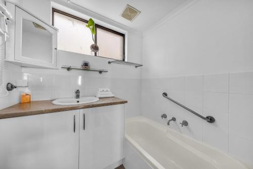 a white bathroom with a sink and a bath tub at Capri Apartments in Merimbula