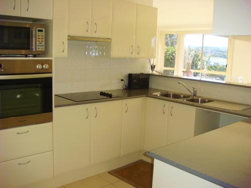 a kitchen with white cabinets and a sink and a microwave at Waterfront Lakeside Cottage Primbee in Primbee