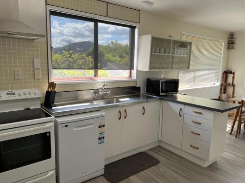 cocina con armarios blancos, fregadero y ventana en Parkview Holiday Home "Opposite of Famous Kuirau Park" en Rotorua