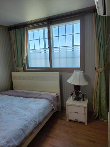 a bedroom with a bed and two windows and a lamp at Capri Hakdong Pension in Geoje 