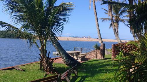 a picnic table and palm trees next to the water at The Lagoon Flat, 53 Nkwazi Drive in Zinkwazi Beach