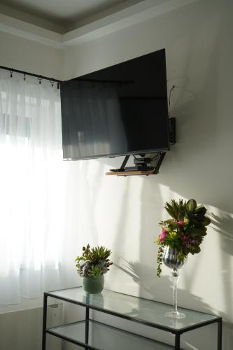 a tv on a wall with flowers on a glass table at Secret Garden Vendégház in Pécs