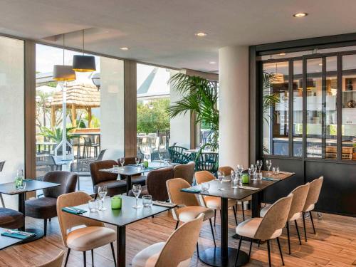 un restaurante con mesas, sillas y ventanas en Novotel La Grande Motte Golf, en La Grande-Motte