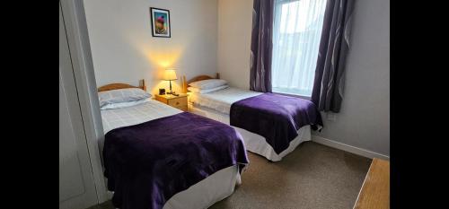 two beds in a room with purple sheets and a window at Inverour Guest House in Spean Bridge