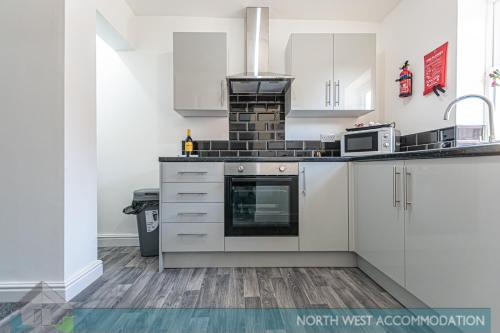 a kitchen with white cabinets and a stove at Wellfield Serviced Accommodation (Warrington) in Warrington