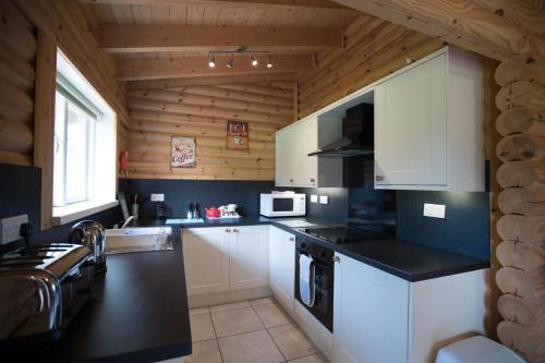 a kitchen with white cabinets and black counter tops at Quail Lodge - Nordic Log Cabin in Selby