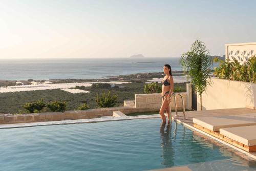 a woman in a bikini standing next to a swimming pool at Falasarna Luxury Villas in Falasarna