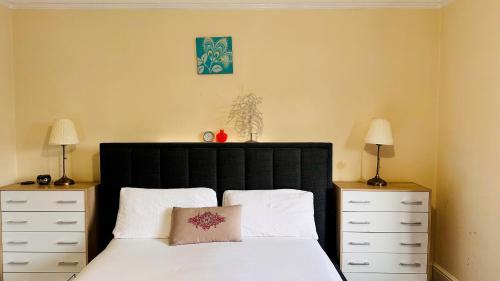 a bedroom with a bed with a black headboard and two dressers at Hestia Travel Slough in Slough