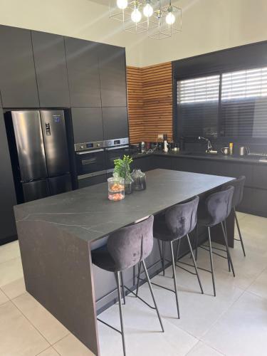 a kitchen with a large black counter with three bar stools at וילת צאלים in Yeroẖam