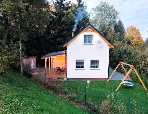 uma pequena casa branca com um parque infantil num quintal em Holiday House Lawendowa Przystań em Miszkowice