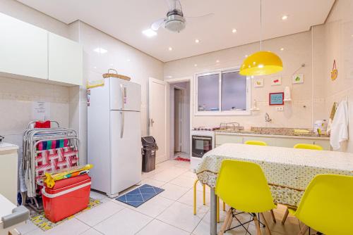 a kitchen with a table and yellow chairs and a refrigerator at Apê Descolado no Guarujá - Enseada in Guarujá