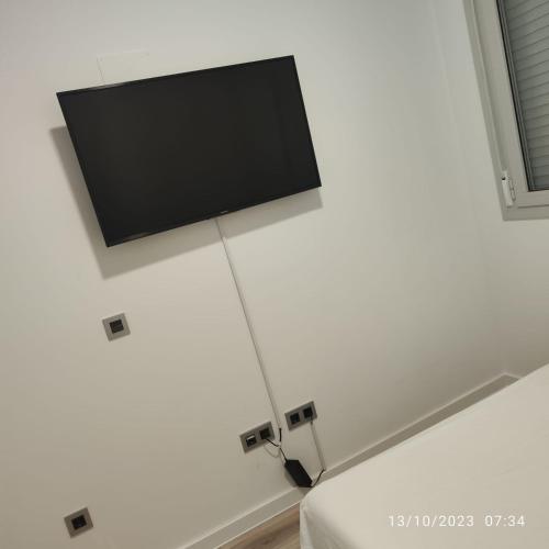 TV de pantalla plana en una pared blanca junto a la cama en Casa particular Tatiana, en Badalona
