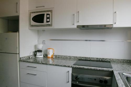 a kitchen with white cabinets and a microwave and a stove at Apartamentos Torre Don Vicente - Arca Rent in Benidorm