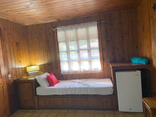 a small bed in a wooden room with a window at Bungalows Malú in Cahuita