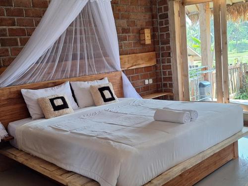 1 dormitorio con 1 cama grande con sábanas y almohadas blancas en Bunga Maliq Bungalow Lombok, en Tetebatu