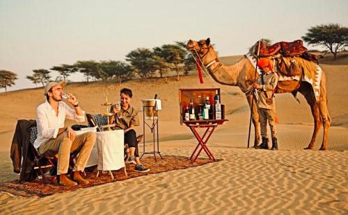 a group of people sitting in the desert with a camel at Sam dunes desert safari camp in Jaisalmer