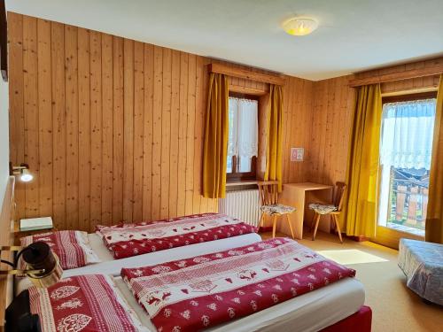 two beds in a room with wooden walls and windows at Albergo Pensione Sport in Arabba