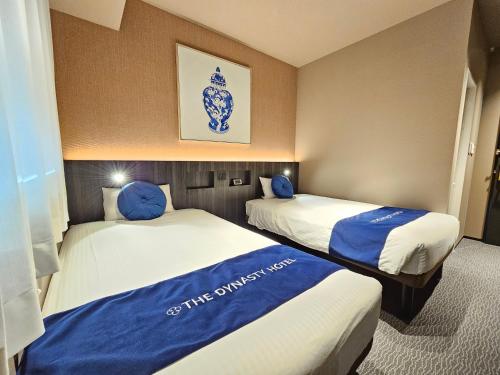 two beds in a hotel room with blue pillows at Dynasty Hotel & Resort Osaka in Osaka