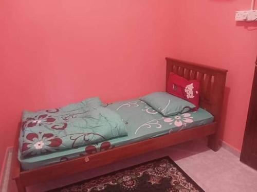 ein kleines Bett in einem Zimmer mit einer rosa Wand in der Unterkunft Homestay kak nun in Kampong Ru Sepuloh