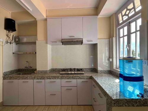 a kitchen with white cabinets and a large window at Ejam House, with a tea garden view in Darjeeling