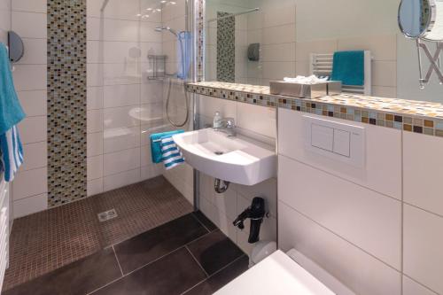 La salle de bains blanche est pourvue d'un lavabo et d'une douche. dans l'établissement Hotel am Elisabethufer, à Jever