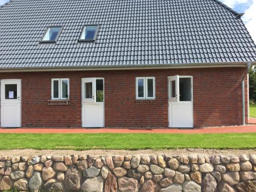 a brick house with white doors and a stone wall at Nije Haven Bed & Breakfast in Wrixum