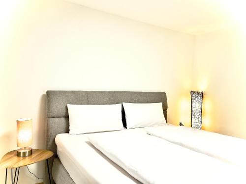 a white bedroom with a bed and a lamp at GastRoom Am Seefeld in Grafing