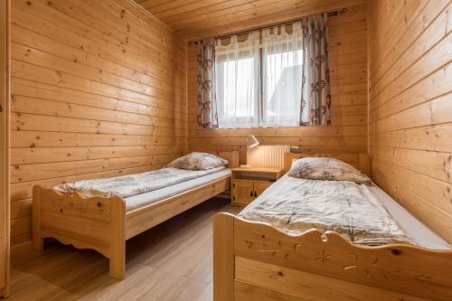 two beds in a wooden room with a window at Domki Pienińskie in Szczawnica