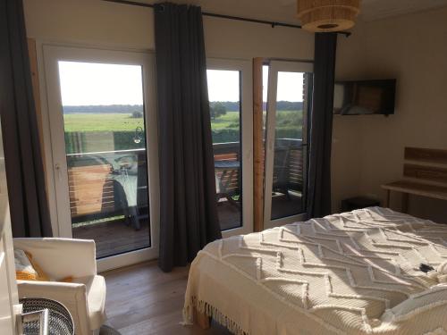 een slaapkamer met een bed en een balkon met glazen schuifdeuren bij Elbauen-Chalet in Cumlosen