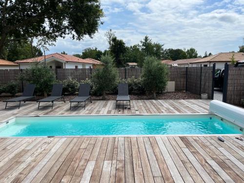une piscine avec des chaises et une terrasse en bois dans l'établissement Maison des landes st Julien en Born Contis, à Saint-Julien-en-Born