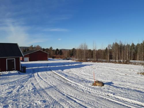 a snow covered field with a barn and a dirt road at Mäki-mummola in Ylitornio