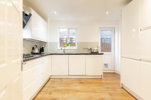 a kitchen with white cabinets and a wooden floor at 5 Bed House Heathrow Egham Virginia Water Sleeps 7 or Up To 8 If Sharing Beds, Mid To Long Term Bookings Welcome in Egham