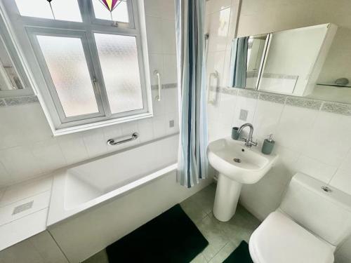 a white bathroom with a sink and a toilet and a tub and a window at 4 Bed house in Daneby Road,SE6 in Catford