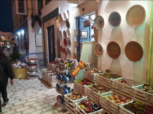 a woman walking past a market with baskets of food at Appartement résidence Port yasmine hammamet in Hammamet
