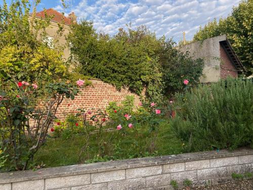 un jardín con rosas rosas y una pared de ladrillo en Studio tt confort neuf et équipé, en Noyon