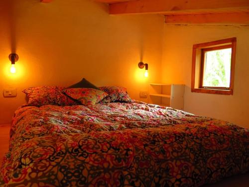1 dormitorio con cama con edredón y ventana en Hermosa casa rodeada de bosque en Los Repollos