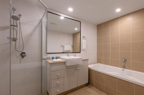 een badkamer met een bad, een wastafel en een douche bij Meriton Suites Broadbeach in Gold Coast
