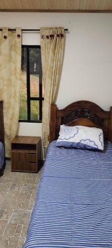 1 dormitorio con 1 cama con edredón azul y ventana en Posada Campestre Macadamia, en Paipa