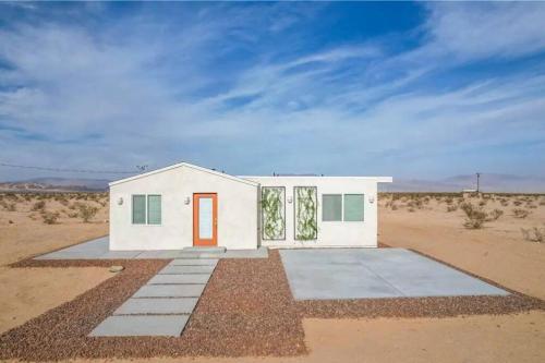 una pequeña casa blanca en medio del desierto en Serene Modern Home Backdoor with great WiFi, games, movies, patio seating and bbq Easy Access to North Joshua Tree National Park in 10 minutes, en Twentynine Palms